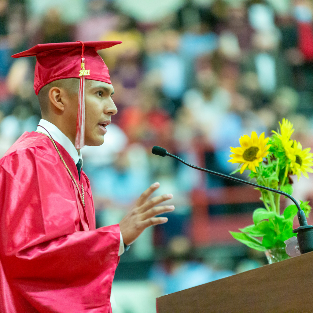 a man in a red cap and gown is giving a speech